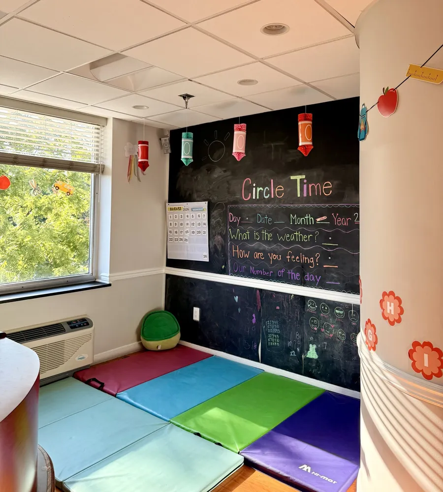 Circle Time room with a chalkboard showing date, weather and feelings prompts over colorful floor mats