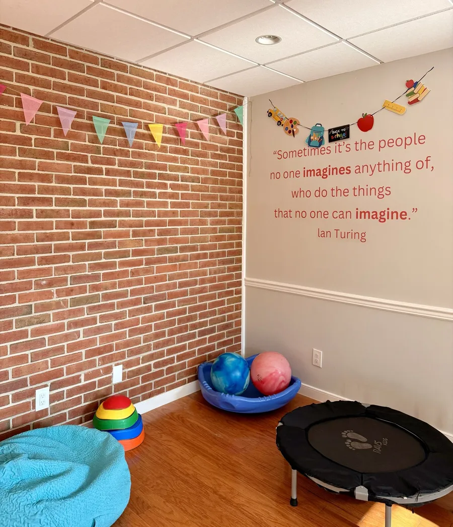 Corner with a brick wall, trampoline, balance toys and an Alan Turing quote about imagination