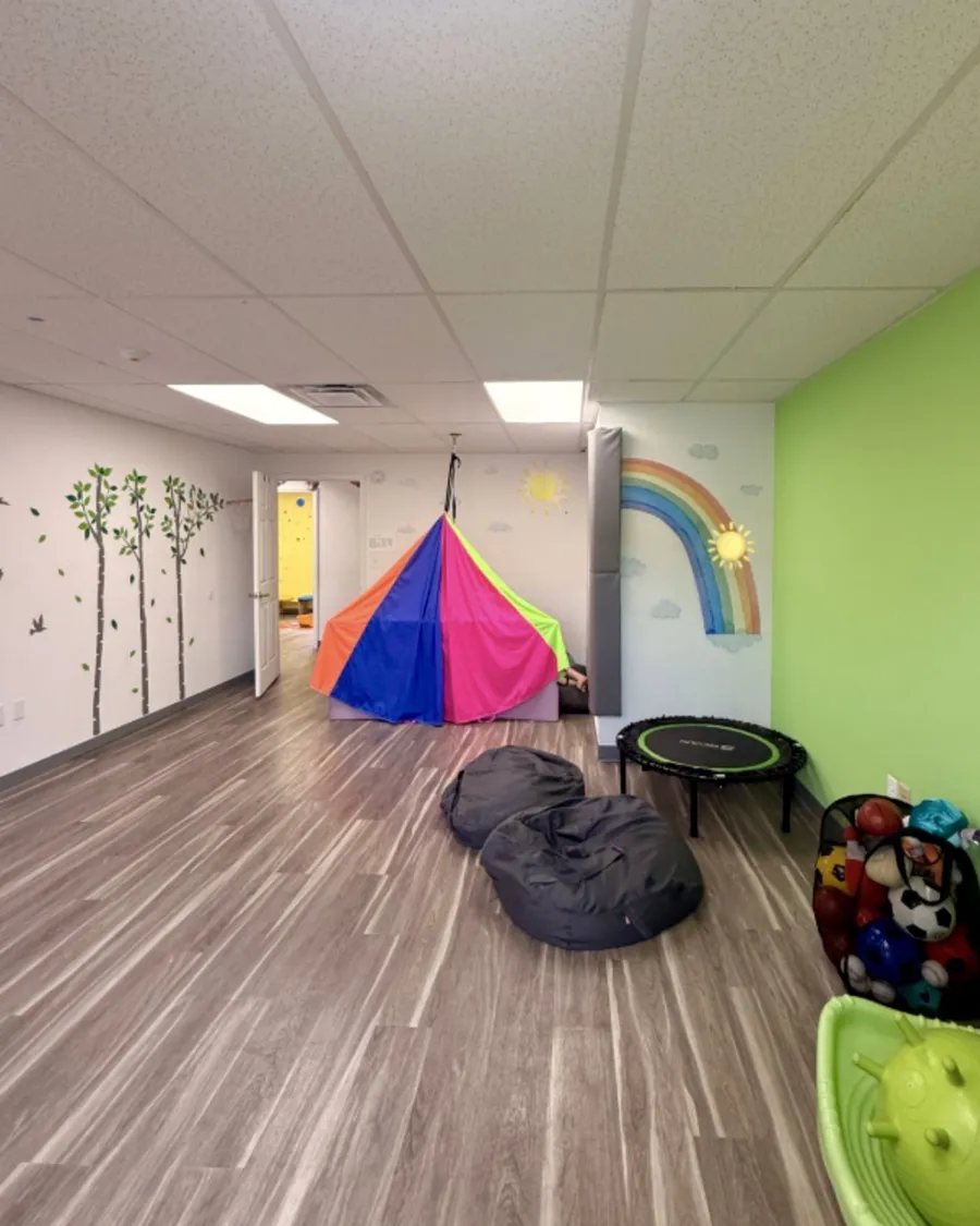 Sensory gym with a rainbow mural, a colorful play tent, bean bags and a small trampoline