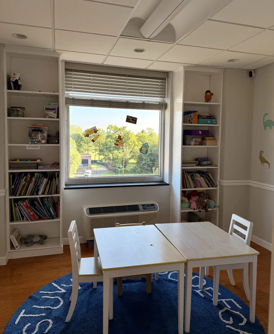Therapy room with a child-size table and chairs, bookshelves and a big window